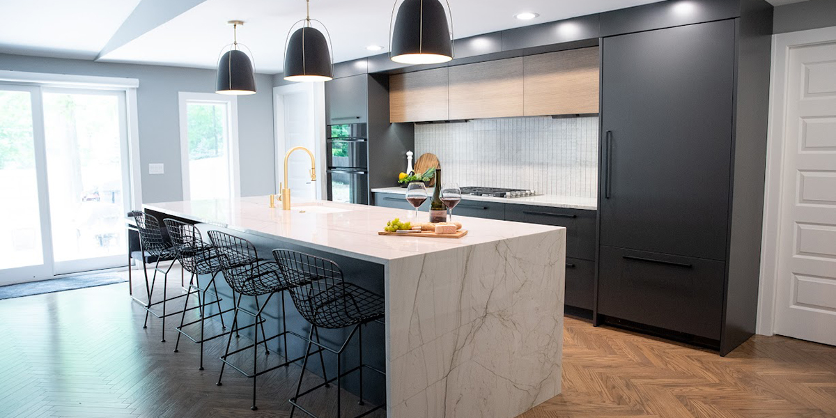 Modern kitchen with a large white marble island, black wire bar stools, and dark gray cabinets; pendant lights overhead.