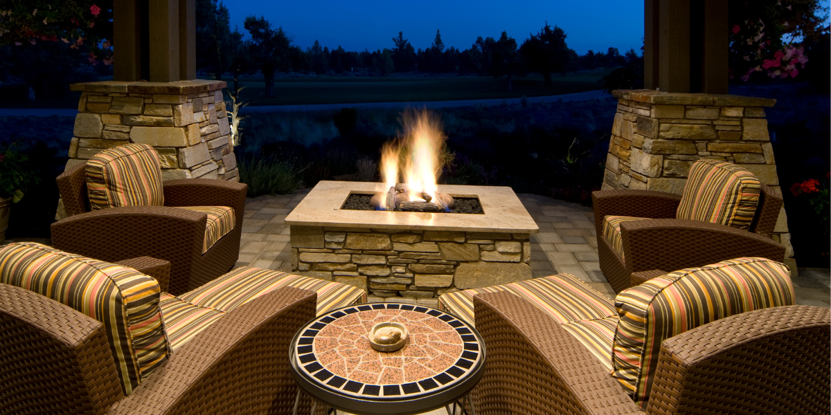 ZStone_FirePits_Feature square stone fire pit lit up at nigh surrounded by patio chairs under cover