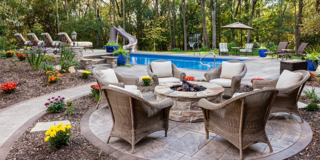 stone fire pits surrounded by chairs on patio with hardscape and pool with slide in background