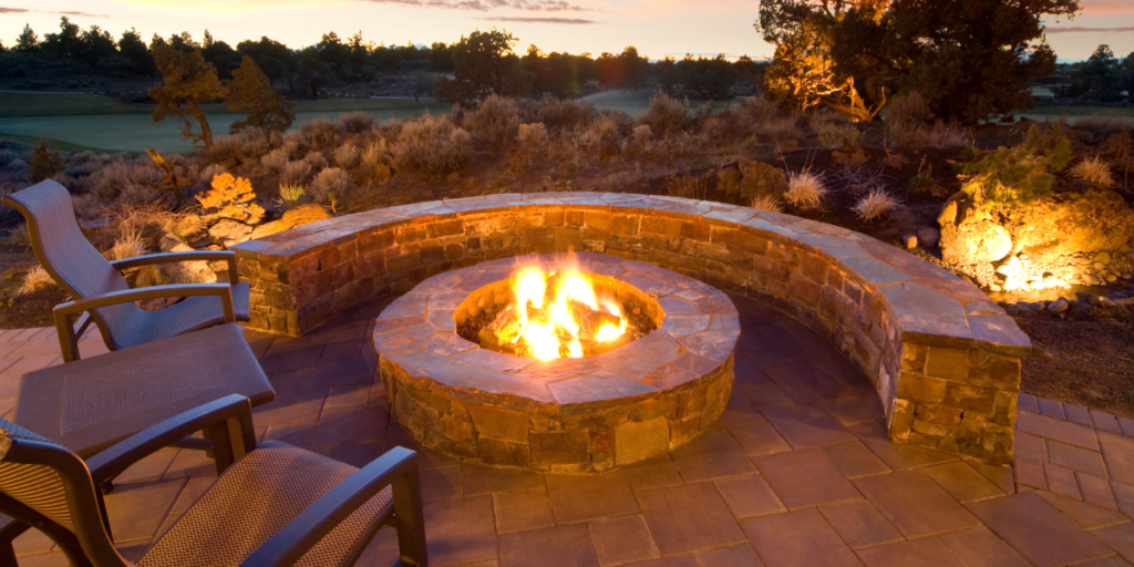 lit, round stone fire pit on patio with curved stone sitting wall during evening
