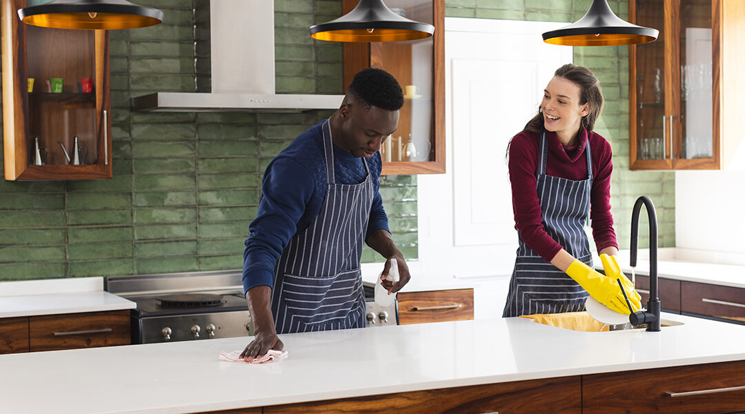 Happy diverse couple cleaning countertop and doing dishes in kitchen at home