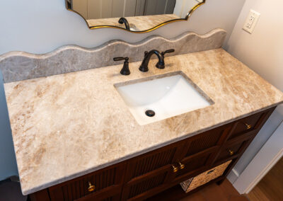 Bathroom vanity with beige marble countertop, undermount sink, and dark bronze faucet.